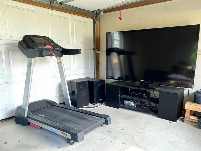 Old treadmill and a large flat screen TV staged in a garage